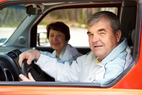 Senior man looking at camera in the car with his wife on background
