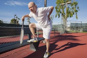 Senior male tennis player with back pain on court