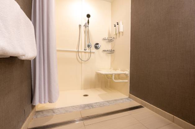 Accessible shower with a folding shower seat, grab bar, and handheld shower with no-threshold entrance and shower curtain