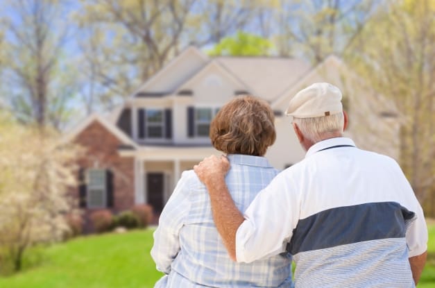 A senior couple looking toward their new home. They are standing in their front yard facing their multistory home.