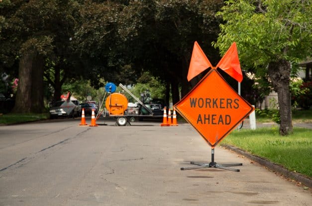 A closed off residential road with a clear view of a large diamond orange sign that says "WORKERS AHEAD."