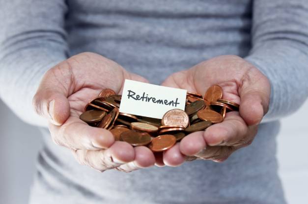 A man wearing a gray shirt is holding a pile of pennies in both hands. There is a sign that says "retirement" in the pile.