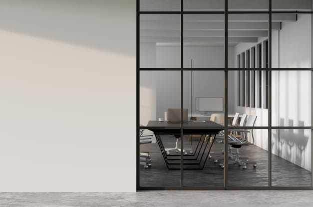 A hallway with white walls and a marble floor in front of a window that shows a meeting room with a table and chairs.