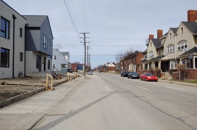 A street in a neighborhood with various two-story homes on both sides and wooden utility poles extending down the left side.