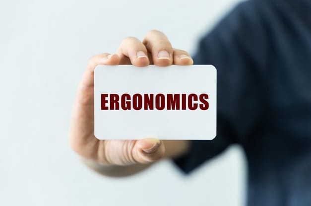 A close-up of a person's hand holding up a plain white card with the word "ergonomics" typed on it in red.