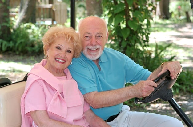 Close-up of a senior man and woman sitting together in a golf cart while smiling and posing for a picture.