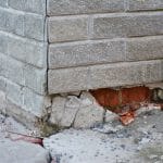 A close up on a home's foundation that is falling apart. The foundation and the wall above it are all cracking apart.