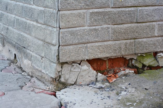 A close up on a home's foundation that is falling apart. The foundation and the wall above it are all cracking apart.